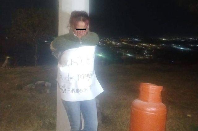 Mujer atada a poste con tanque de gas a un lado 