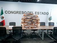 Foto del Congreso del estado y encima de un escritorio, folders con documentos, apilados
